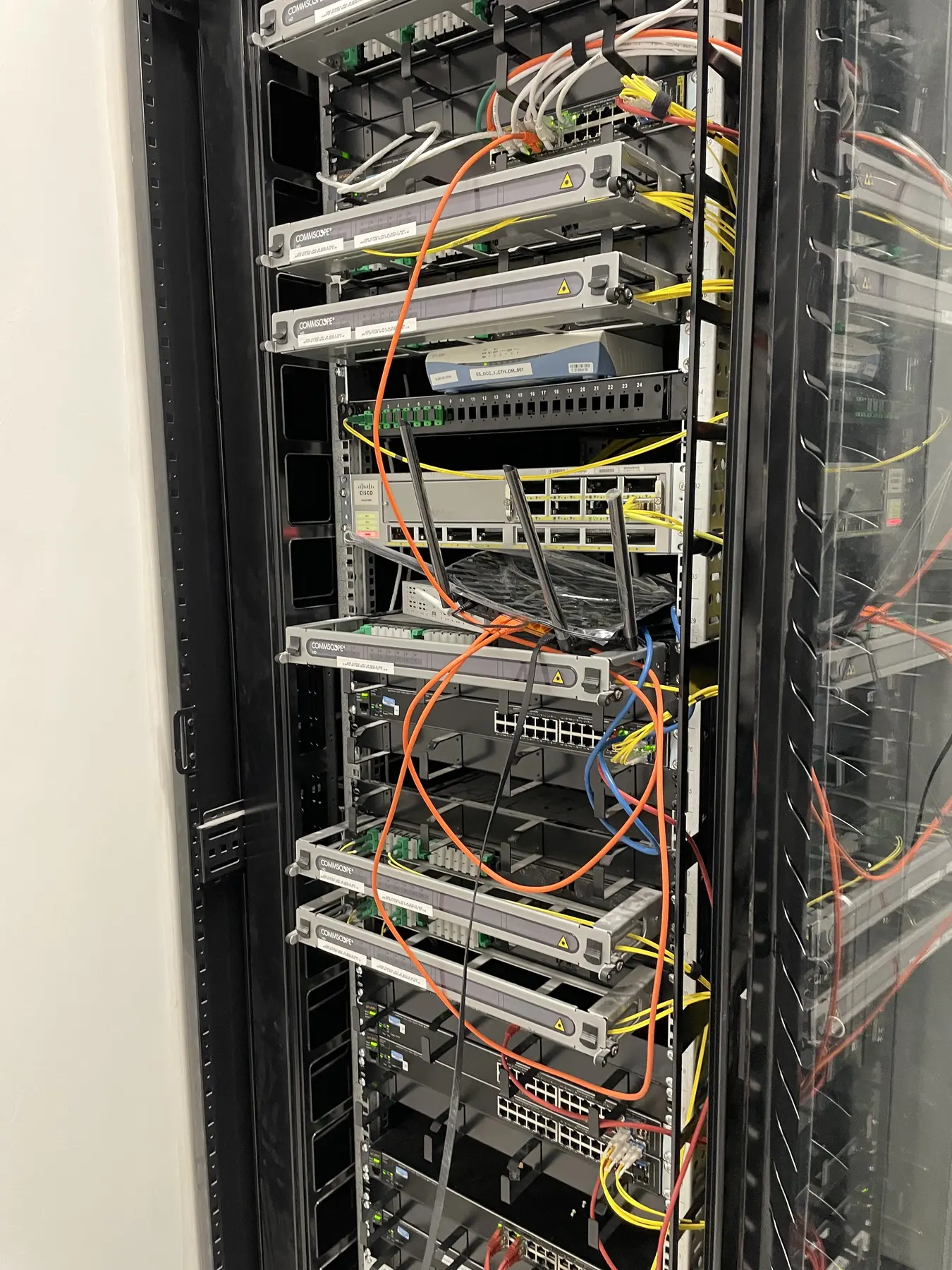 Network equipment racks with visible orange, yellow, and blue cabling in a data room
