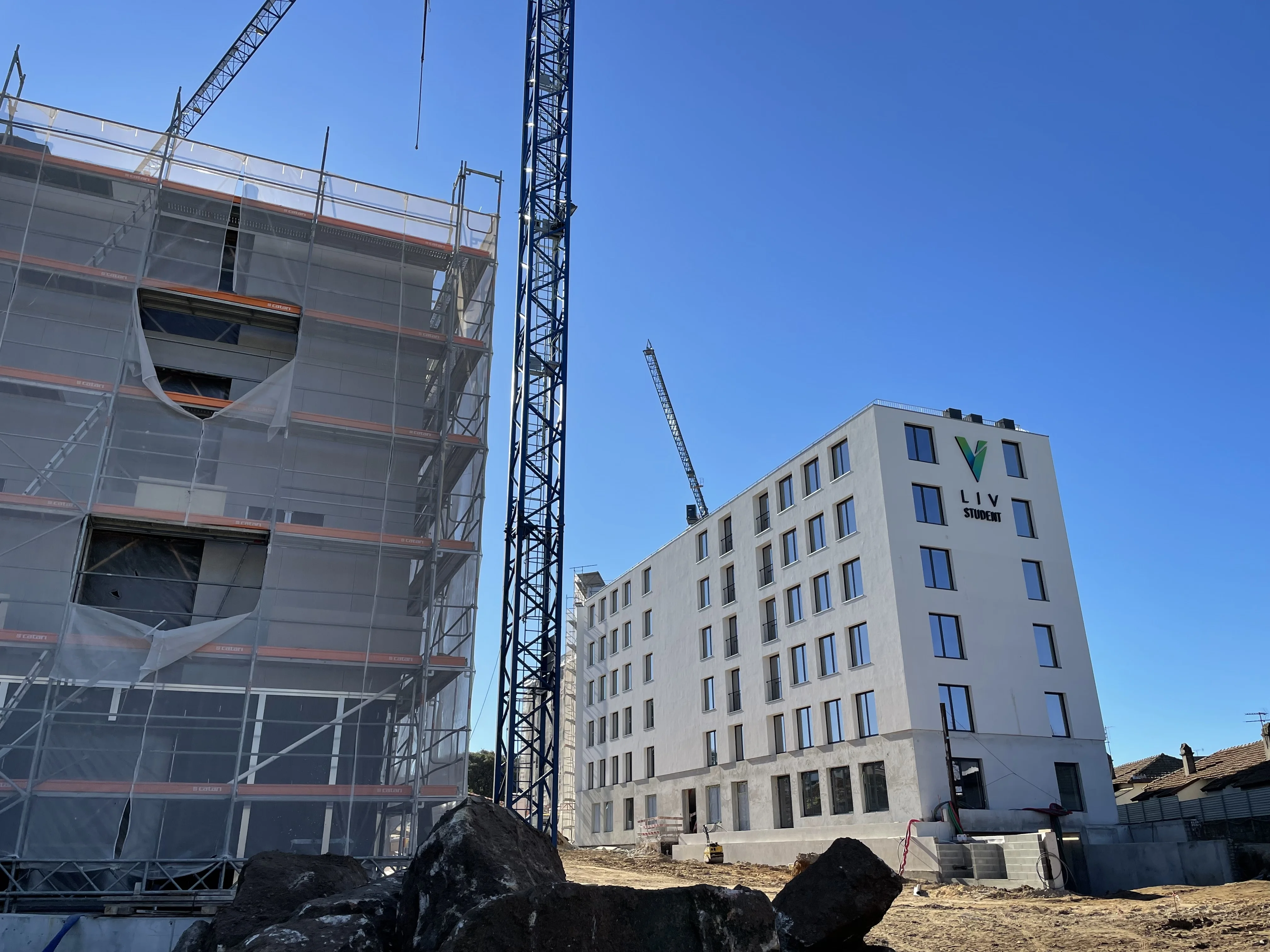 Student residence under construction beside a completed building, with cranes against a clear sky