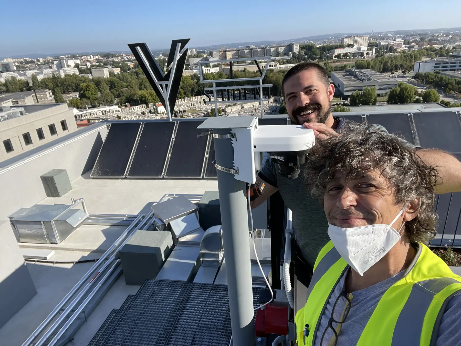 Two project team members on a rooftop beside building equipment, with the surrounding city visible behind them